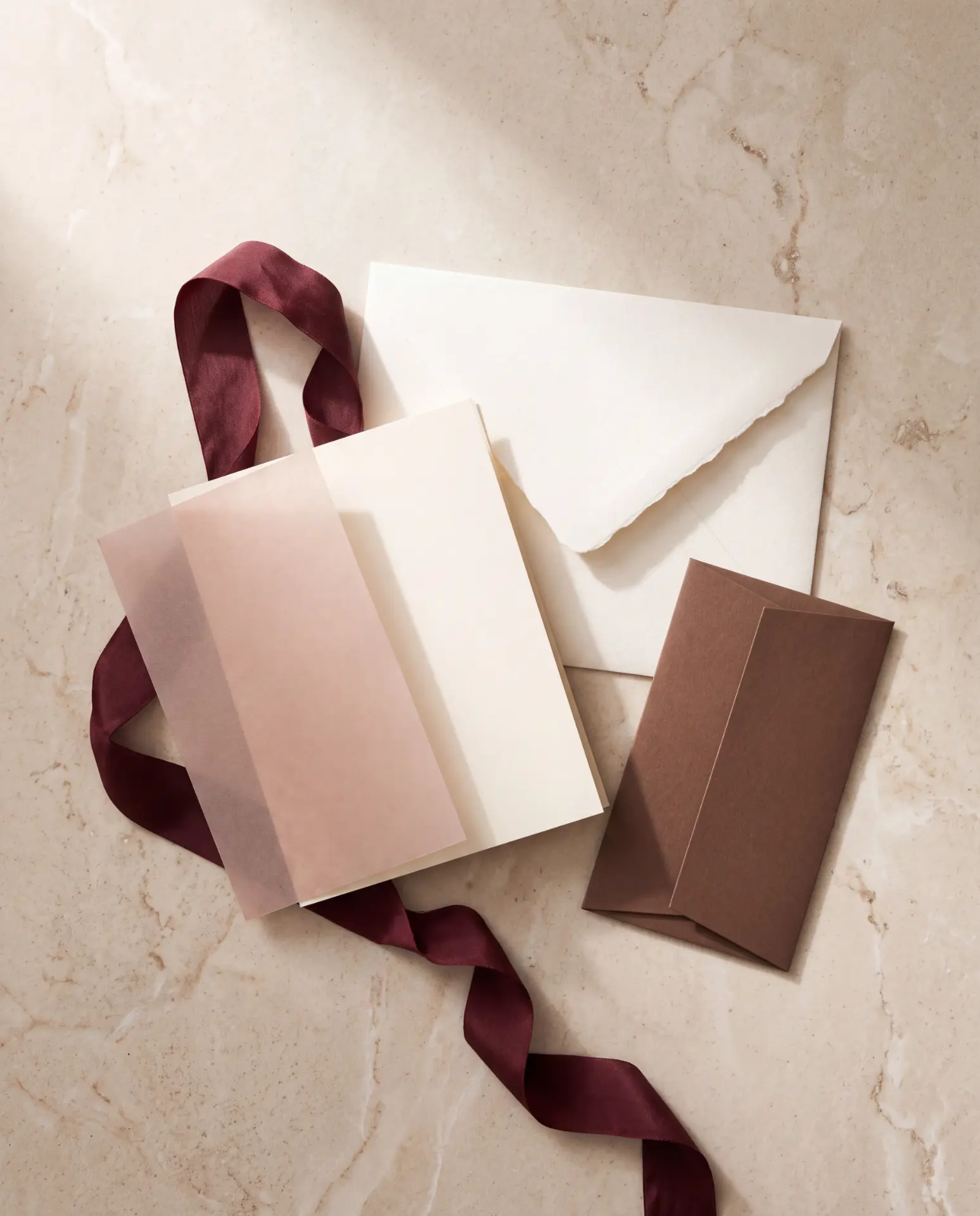Ivory and blush envelopes with a burgundy ribbon on marble