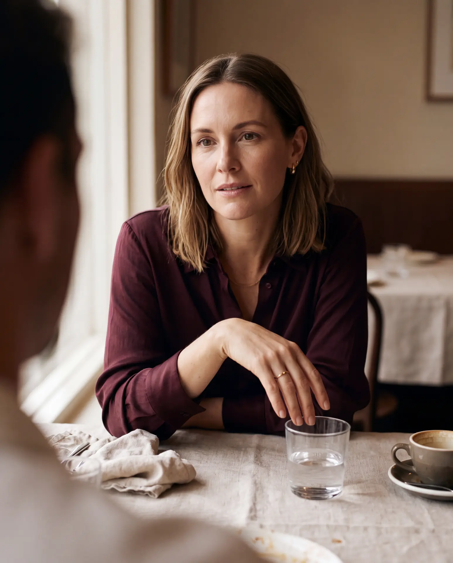 A woman listening across a lunch table by a window